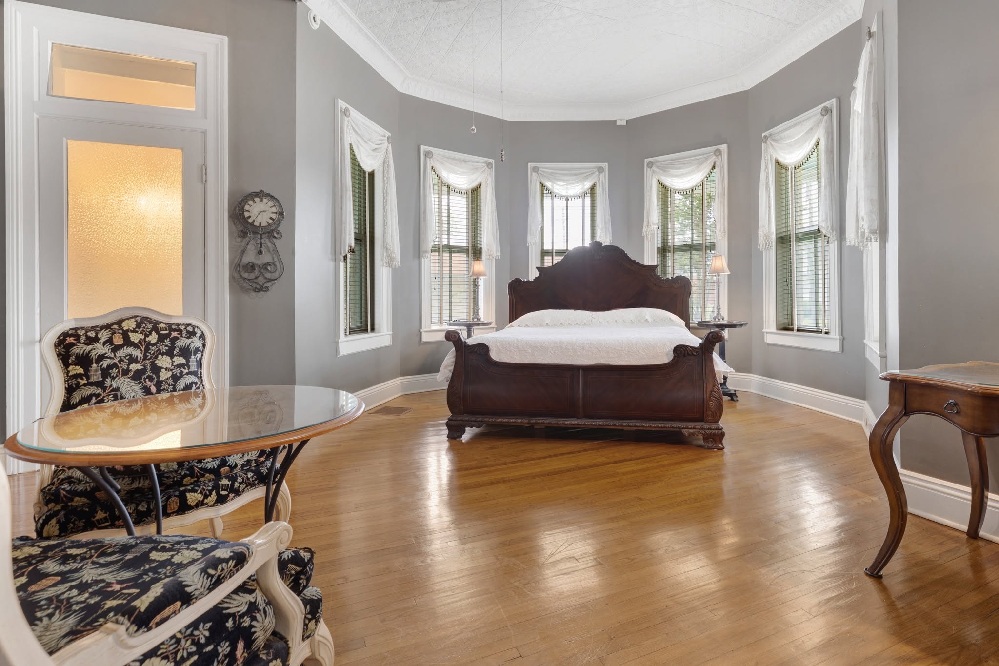 A guest suite — carved dark-wood king bed beneath a curved bay of lace-swagged windows