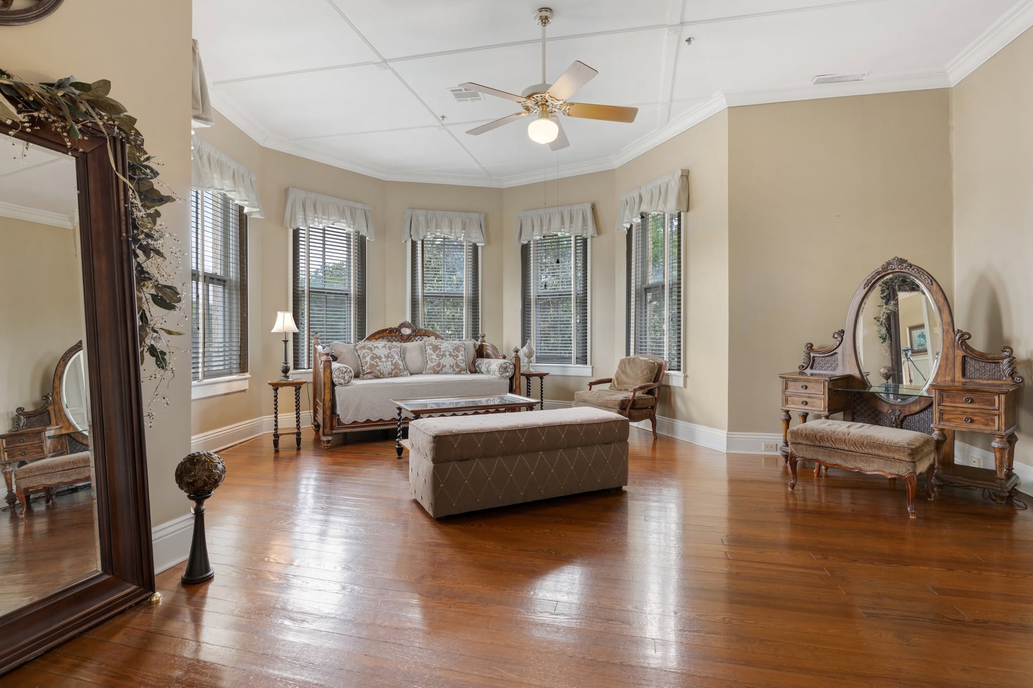 A suite sitting room — antique settee, floor mirror, and vanity in bay-window light