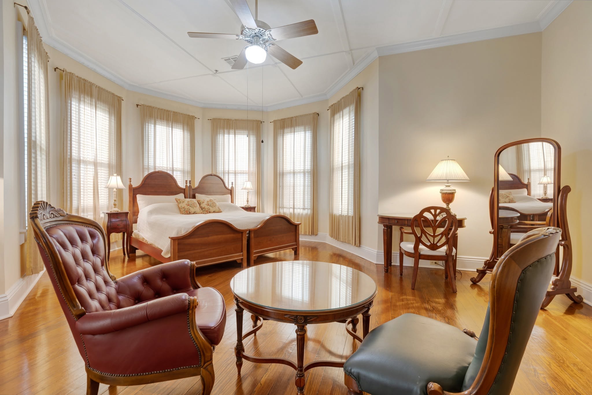 A guest room with twin arched wood beds and a curtained bay of windows