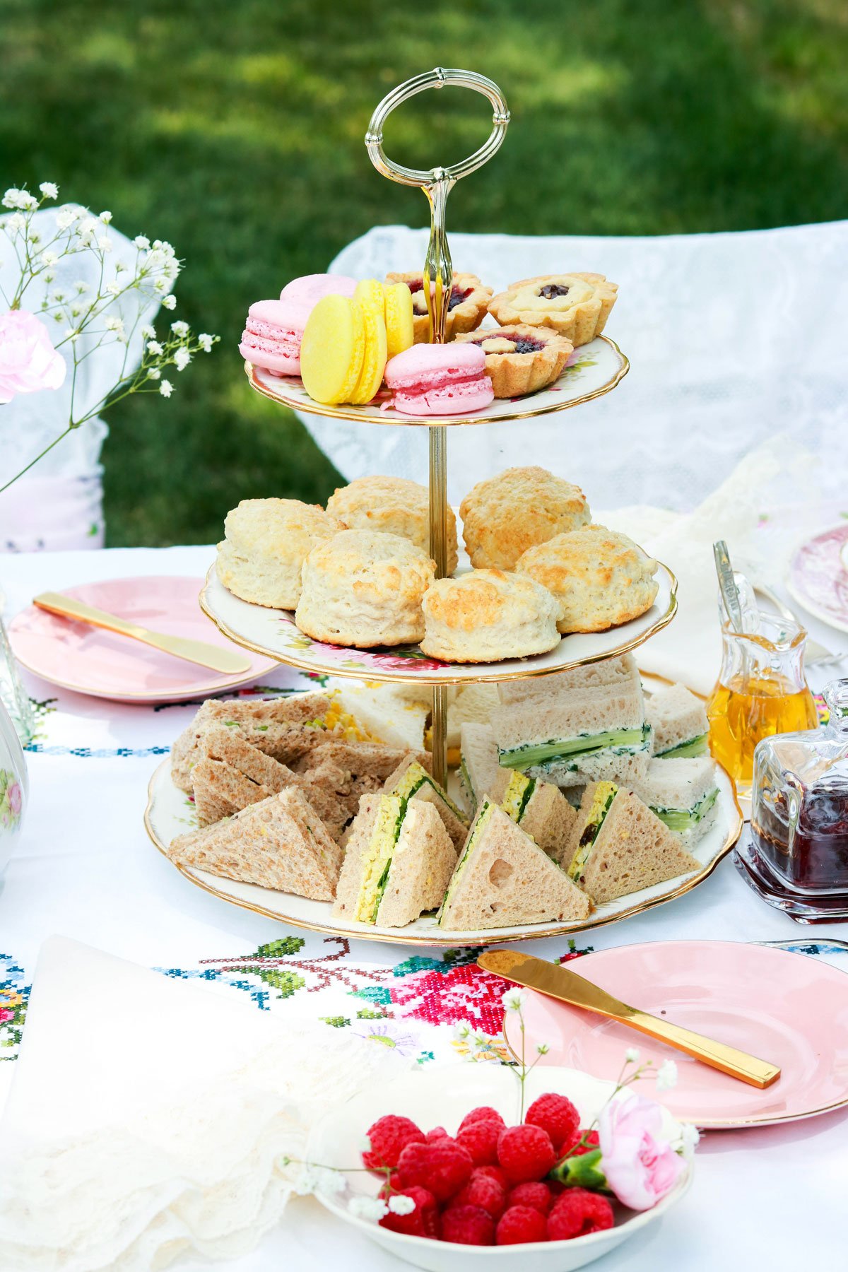 A garden tea at The Caldwell House — a tiered stand of macarons, scones, and tea sandwiches with fine china, gold flatware, and soft florals on a lace-laid table