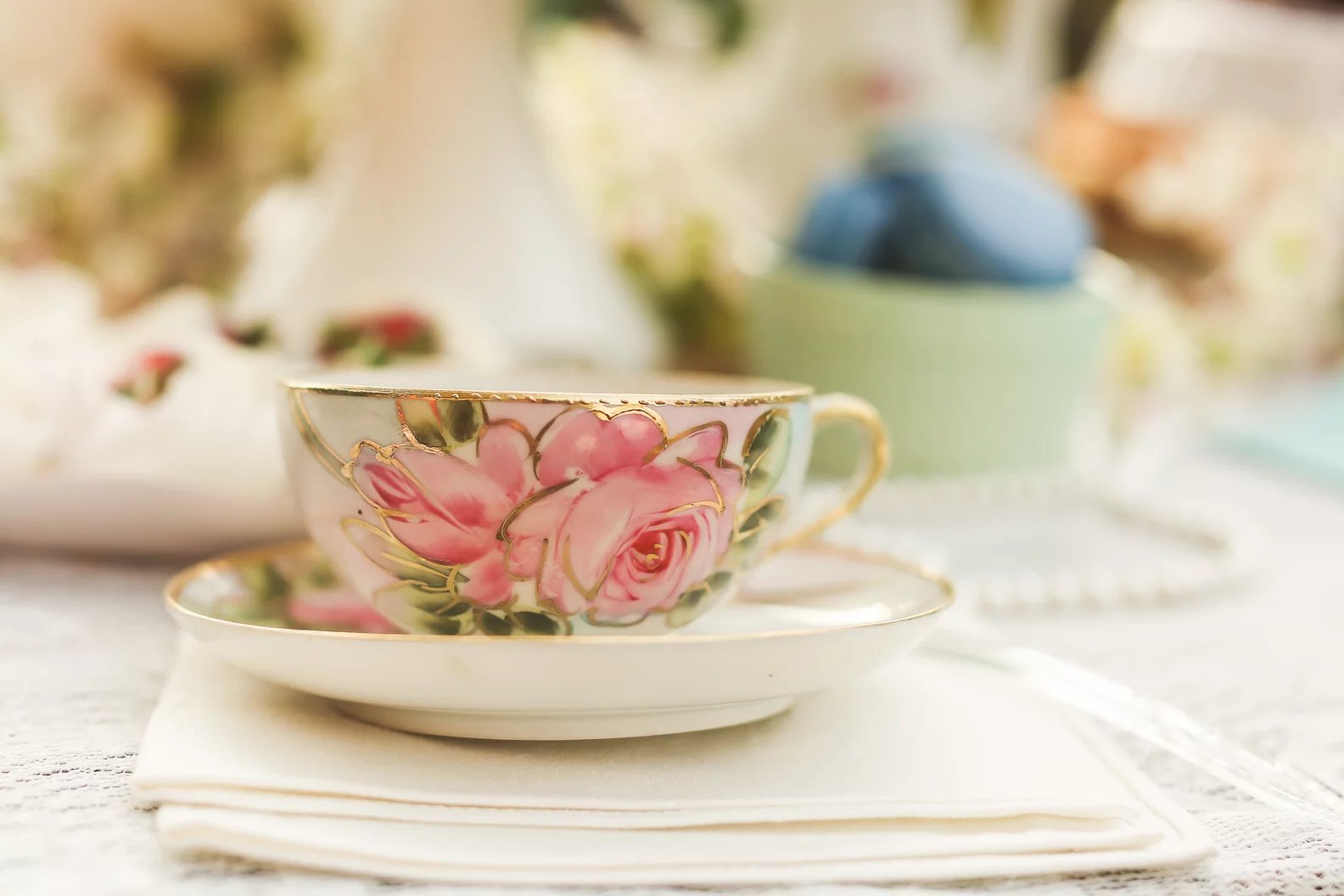 An heirloom rose-painted teacup and saucer on lace linens — the good china set for a shower at The Caldwell House